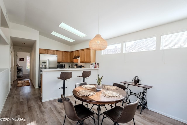 dining space featuring hardwood / wood-style flooring and vaulted ceiling with skylight