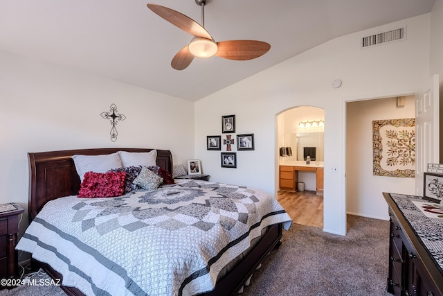 bedroom with ceiling fan, ensuite bathroom, vaulted ceiling, and light carpet