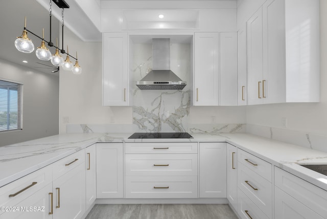 kitchen with white cabinets, wall chimney range hood, hanging light fixtures, light stone countertops, and black electric cooktop