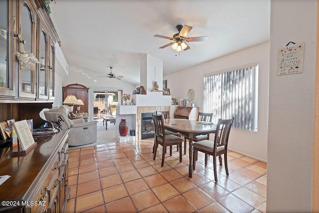 dining room featuring a tile fireplace, ceiling fan, light tile patterned flooring, and lofted ceiling