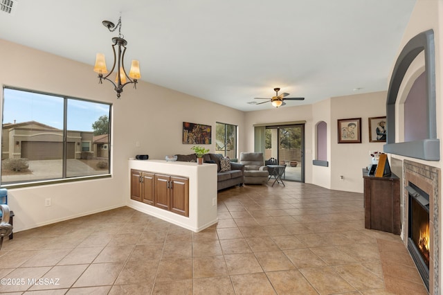 tiled living room with ceiling fan with notable chandelier and a tile fireplace