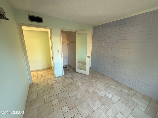 unfurnished bedroom featuring a closet, brick wall, and a textured ceiling