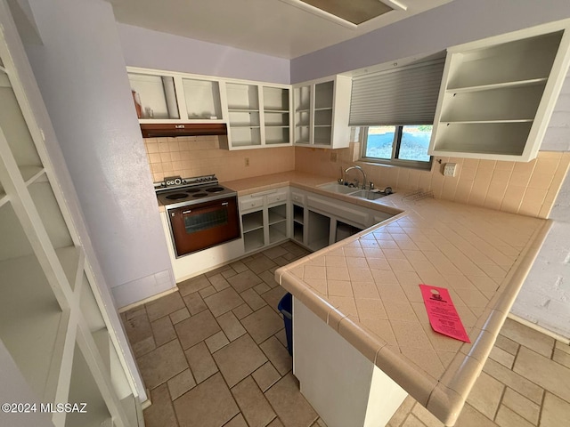 kitchen with backsplash, sink, tile countertops, white cabinetry, and oven