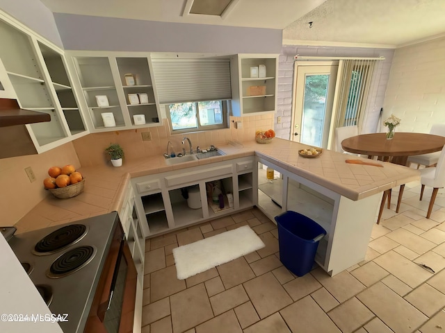 kitchen with kitchen peninsula, a wealth of natural light, tile counters, and sink