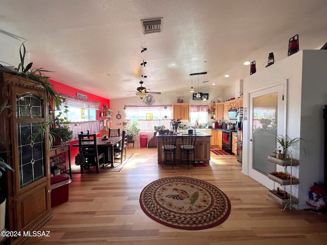 interior space featuring a kitchen bar, ceiling fan, light hardwood / wood-style flooring, a center island, and black / electric stove