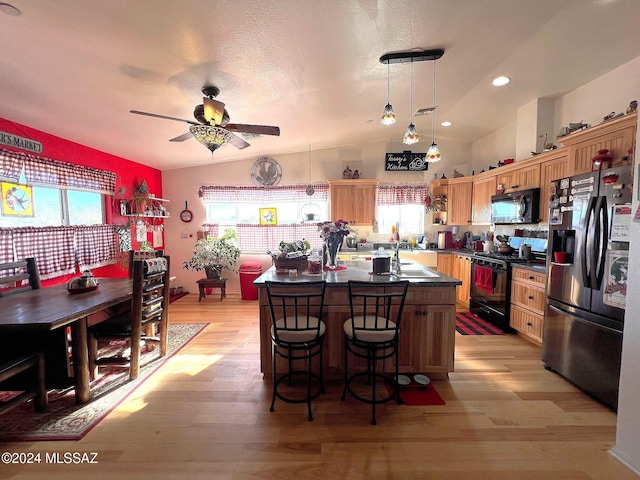 kitchen featuring sink, black appliances, pendant lighting, light hardwood / wood-style flooring, and a kitchen island