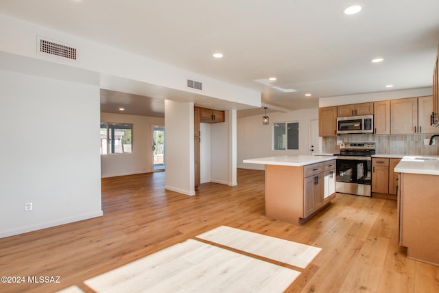 kitchen with decorative backsplash, appliances with stainless steel finishes, a center island, and light hardwood / wood-style flooring