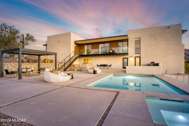 back house at dusk with a balcony, an outdoor hangout area, and a patio area