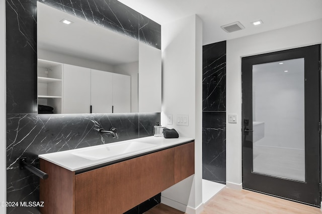 bathroom with hardwood / wood-style flooring, vanity, tile walls, and decorative backsplash