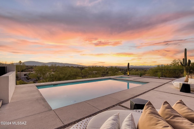 pool at dusk with an in ground hot tub, a mountain view, and a patio