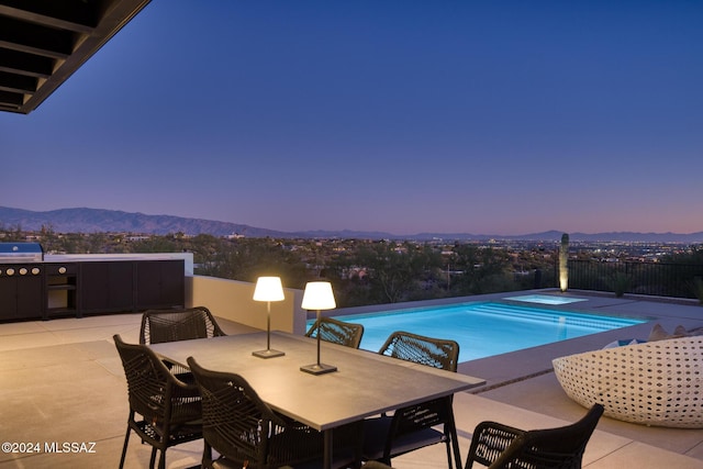 pool at dusk with an in ground hot tub, a mountain view, area for grilling, and a patio area