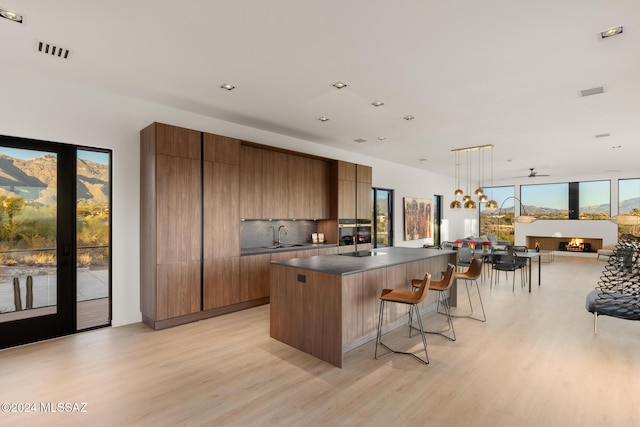 kitchen with hanging light fixtures, backsplash, light hardwood / wood-style floors, and a center island with sink