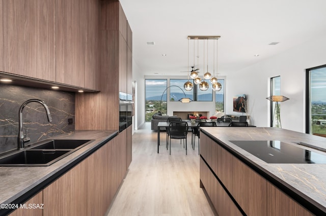 kitchen featuring sink, an inviting chandelier, hanging light fixtures, black electric stovetop, and light hardwood / wood-style floors