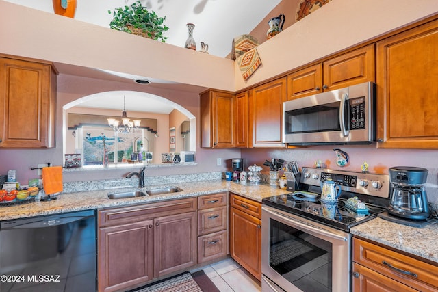 kitchen with sink, light tile patterned floors, appliances with stainless steel finishes, a notable chandelier, and light stone counters