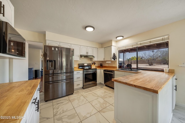 kitchen with stainless steel appliances, a sink, marble finish floor, butcher block counters, and under cabinet range hood