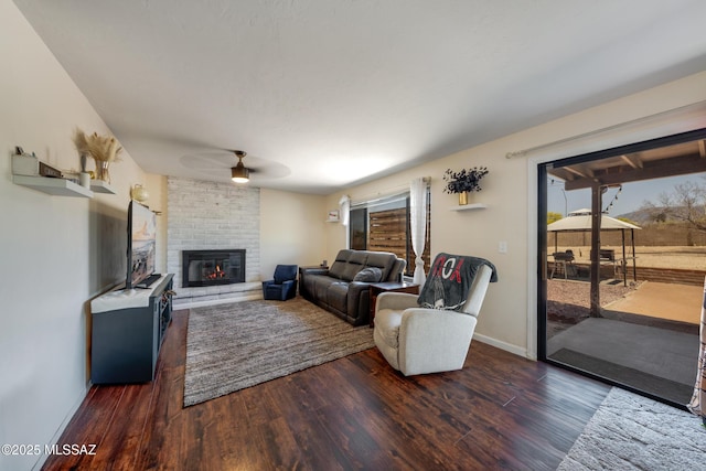 living area featuring a brick fireplace, wood finished floors, a healthy amount of sunlight, and a ceiling fan