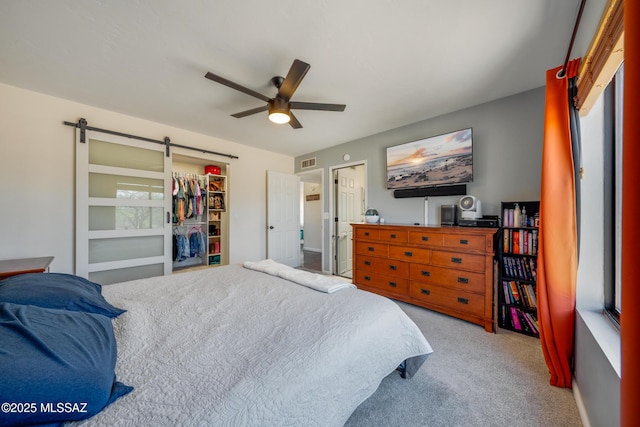 carpeted bedroom featuring a barn door, visible vents, a spacious closet, a ceiling fan, and a closet