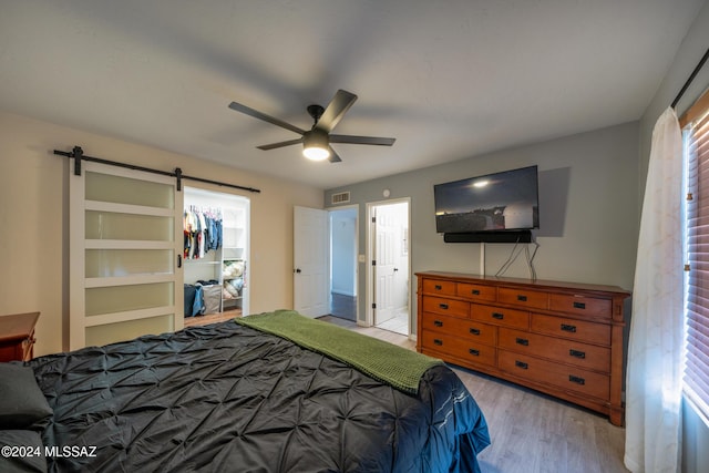 bedroom featuring a barn door, a closet, ceiling fan, and light hardwood / wood-style floors