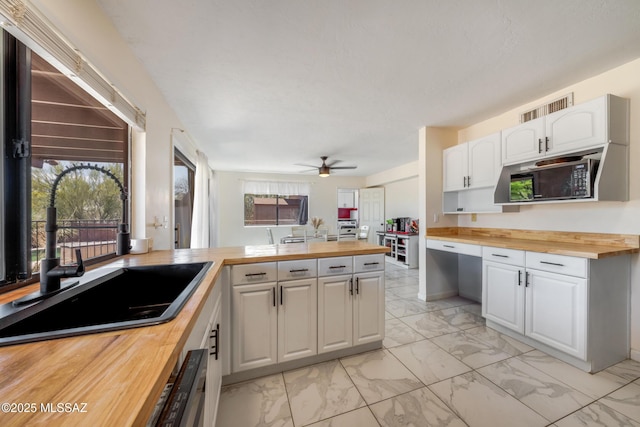 kitchen featuring a sink, marble finish floor, ceiling fan, butcher block counters, and visible vents