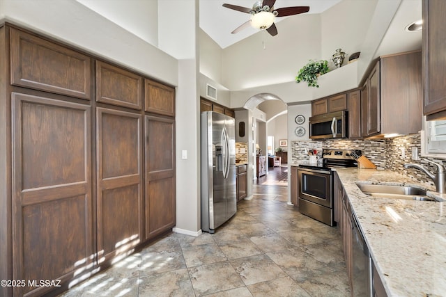 kitchen featuring light stone countertops, appliances with stainless steel finishes, decorative backsplash, sink, and high vaulted ceiling