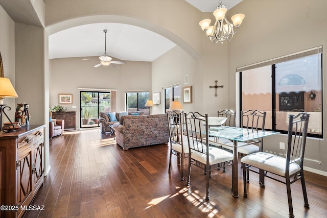 dining space with dark wood-type flooring, ceiling fan with notable chandelier, and high vaulted ceiling