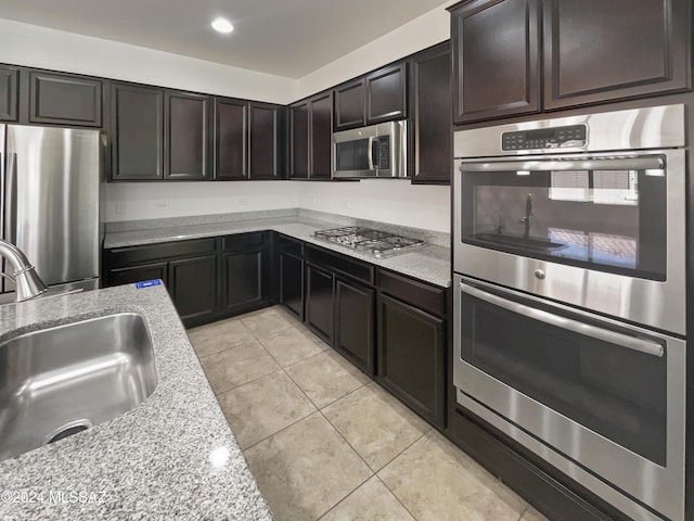 kitchen with light stone countertops, sink, stainless steel appliances, dark brown cabinets, and light tile patterned flooring