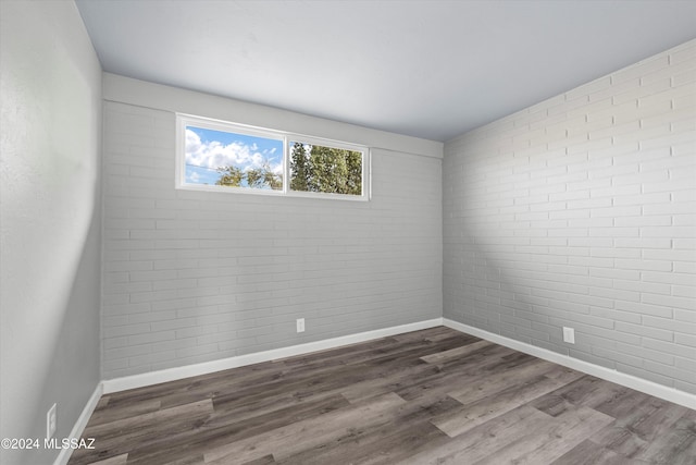 spare room with dark hardwood / wood-style flooring and brick wall