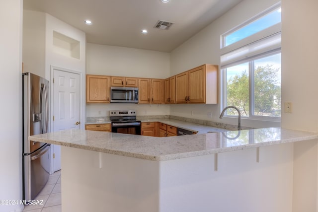 kitchen with a kitchen breakfast bar, light stone counters, kitchen peninsula, and appliances with stainless steel finishes