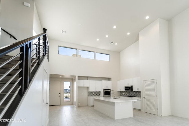 kitchen featuring white cabinetry, a center island with sink, a towering ceiling, and appliances with stainless steel finishes