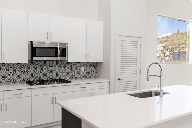 kitchen featuring a kitchen island with sink, sink, decorative backsplash, white cabinetry, and stainless steel appliances