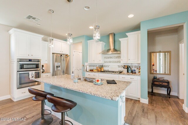 kitchen featuring pendant lighting, wall chimney exhaust hood, sink, and stainless steel appliances