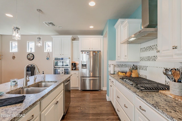 kitchen featuring pendant lighting, white cabinets, wall chimney range hood, sink, and stainless steel appliances