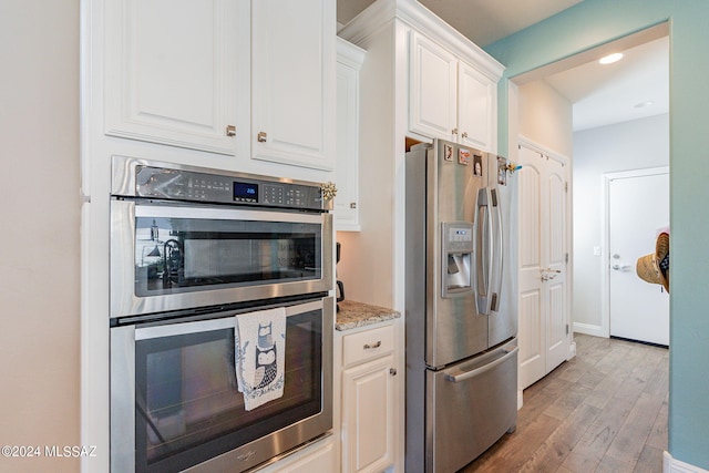 kitchen with white cabinets, light stone counters, stainless steel appliances, and light hardwood / wood-style flooring