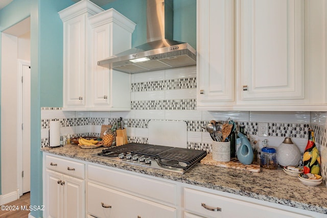 kitchen with white cabinets, wall chimney exhaust hood, decorative backsplash, light stone counters, and stainless steel gas cooktop