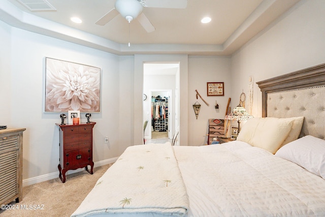 carpeted bedroom featuring a tray ceiling, a spacious closet, a closet, and ceiling fan