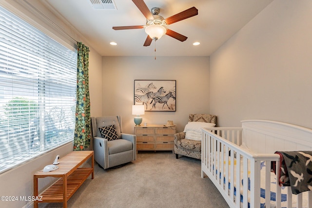 carpeted bedroom featuring a crib and ceiling fan