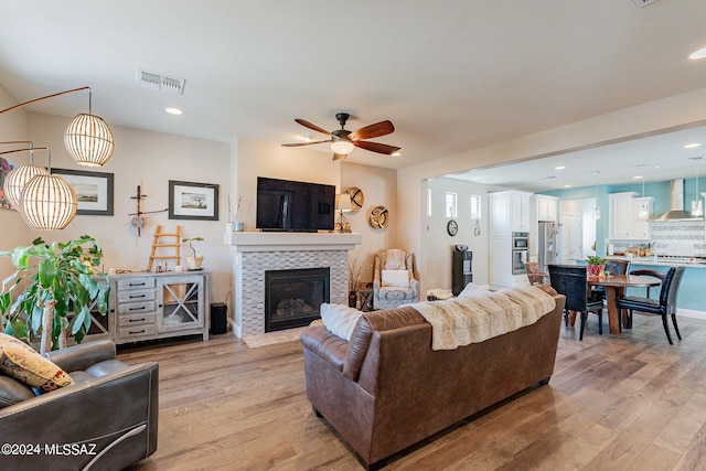 living room with a tiled fireplace, ceiling fan, and light hardwood / wood-style flooring