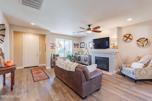 living room featuring light hardwood / wood-style flooring, ceiling fan, and a tiled fireplace