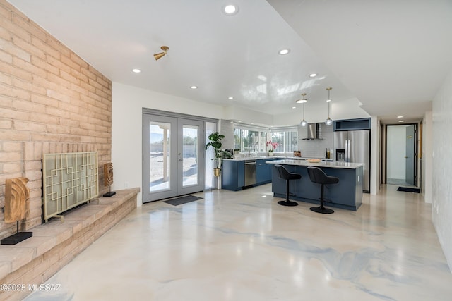 kitchen with decorative light fixtures, a center island, wall chimney exhaust hood, french doors, and a kitchen breakfast bar