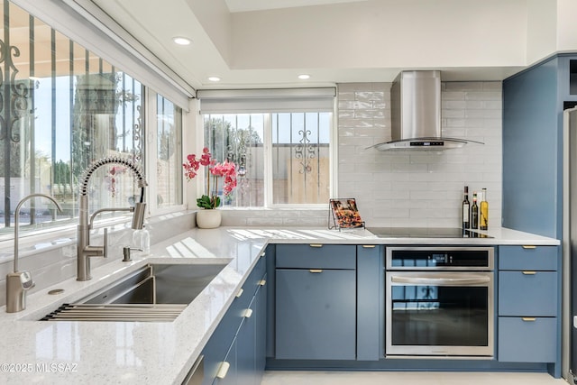 kitchen featuring blue cabinetry, black electric stovetop, sink, oven, and wall chimney range hood