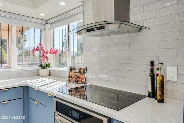 kitchen featuring island range hood, black electric cooktop, light stone counters, oven, and blue cabinets