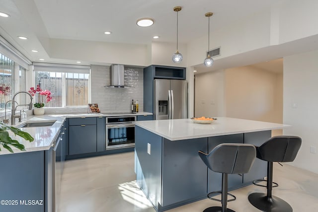 kitchen with stainless steel appliances, sink, blue cabinetry, a kitchen island, and wall chimney range hood