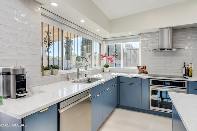 kitchen with sink, decorative backsplash, blue cabinetry, wall chimney range hood, and appliances with stainless steel finishes