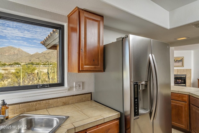 kitchen with stainless steel fridge, sink, a mountain view, tile counters, and a tiled fireplace