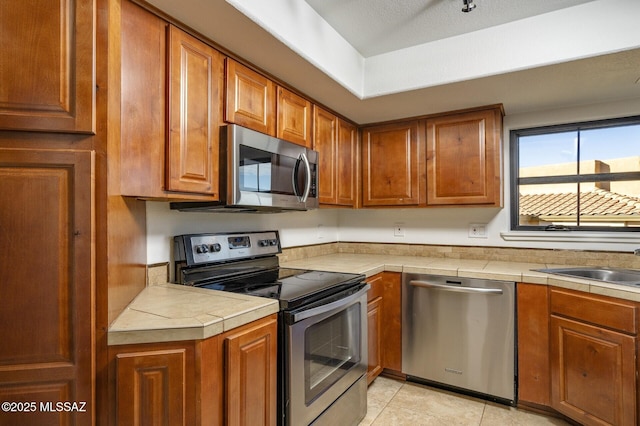 kitchen with tile counters, sink, light tile patterned floors, and stainless steel appliances