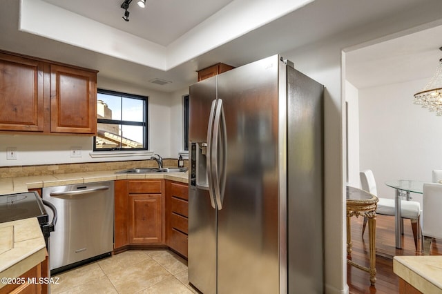 kitchen with sink, appliances with stainless steel finishes, a tray ceiling, tile counters, and light tile patterned flooring