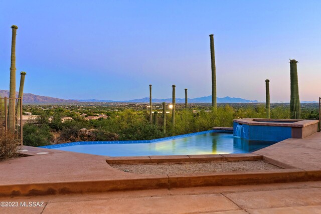 pool at dusk with a mountain view and an in ground hot tub