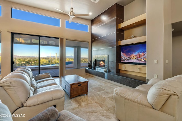 living room featuring ceiling fan, a wealth of natural light, a premium fireplace, and a high ceiling