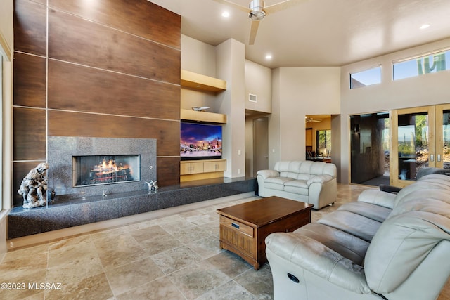 living room featuring a high ceiling, built in features, ceiling fan, and a tiled fireplace