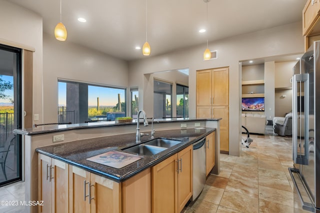 kitchen featuring dark stone counters, stainless steel appliances, sink, decorative light fixtures, and an island with sink